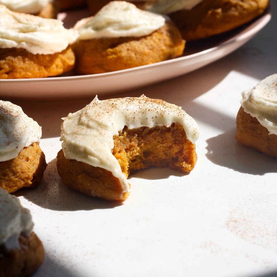 Soft pumpkin cookies on a white counter next to a pink plate