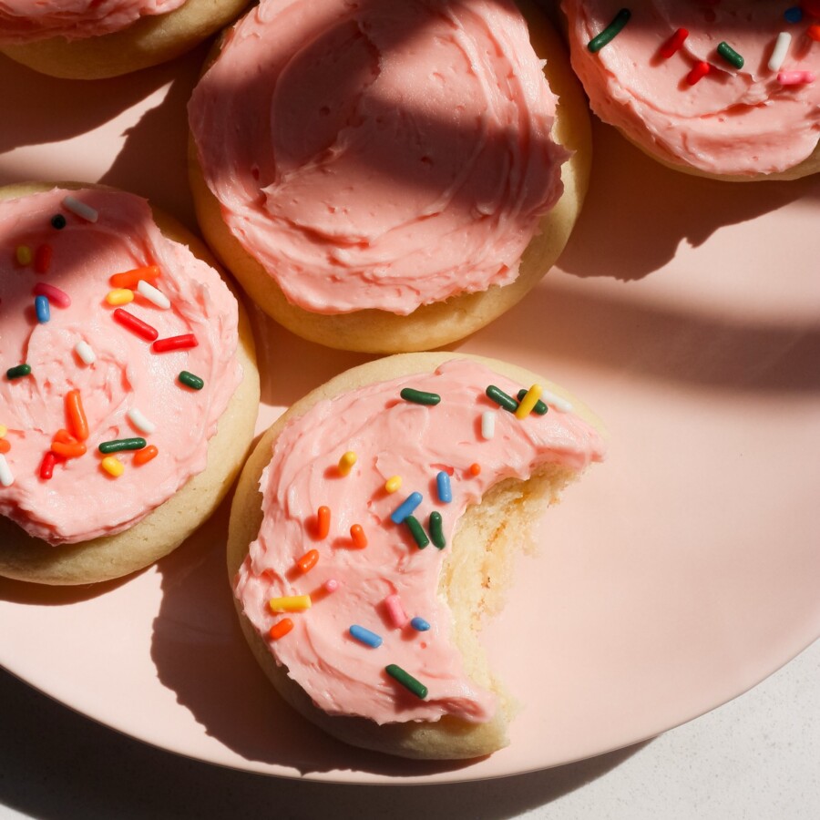 Close up shot of soft frosted sugar cookies on a pink plate in direct sunlight on a kitchen counter