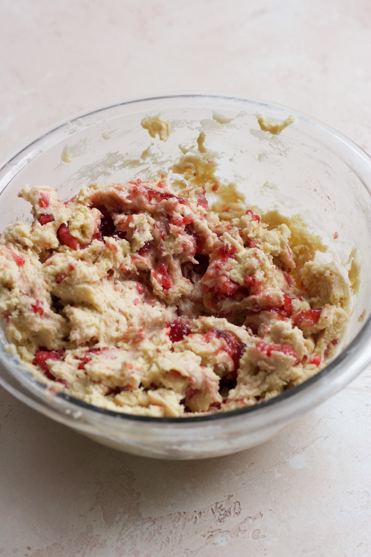 Raspberry muffin cookie dough in a glass bowl on a pink backdrop