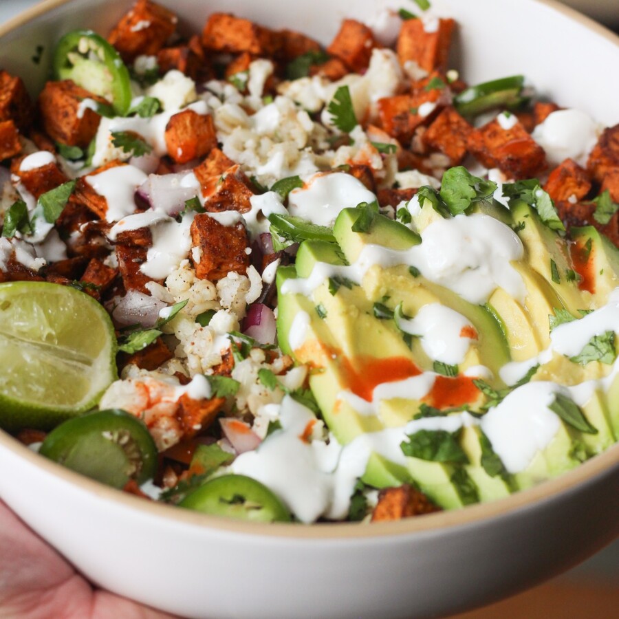 Bowl of roasted sweet potatoes with brown rice, red onion, avocado, and cilantro.