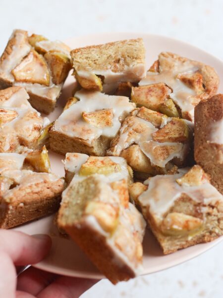 Tyler, author of Schmidty Bakes, holding a pink plate with sliced apple fritter bars.