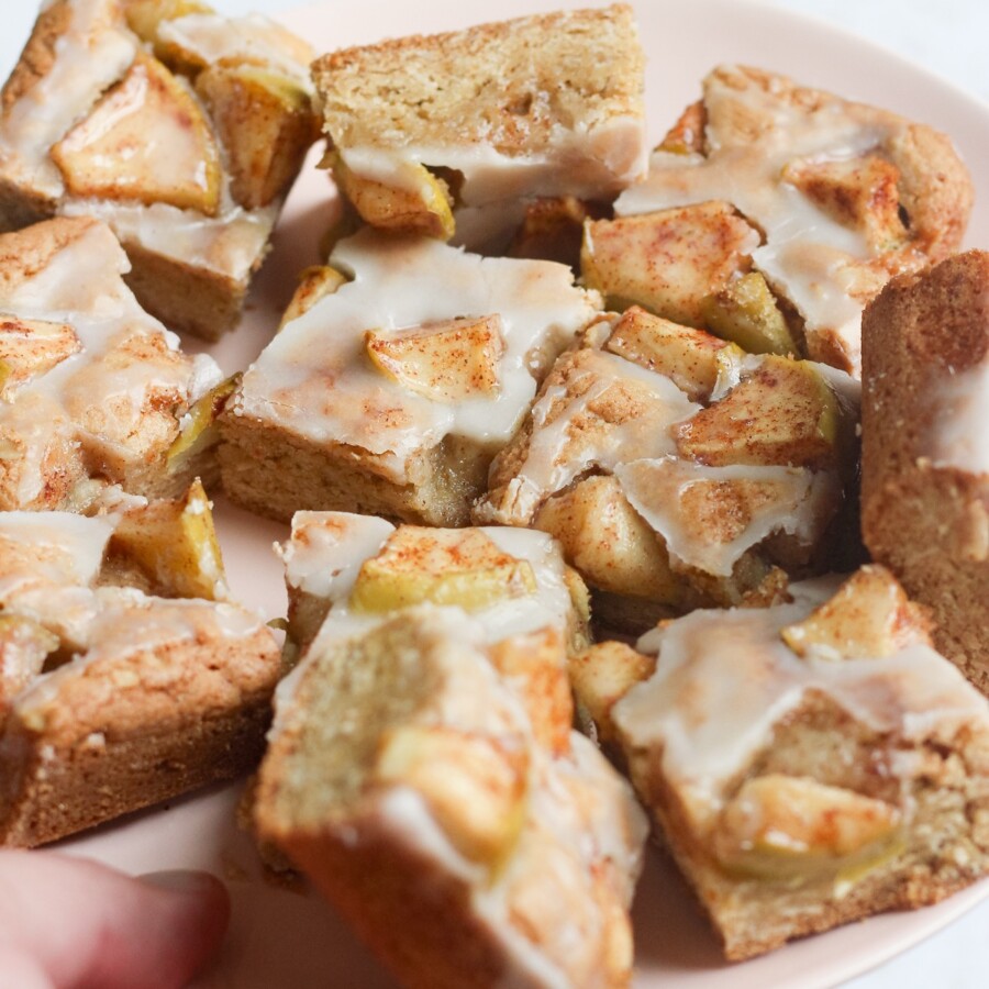 Tyler, author of Schmidty Bakes, holding a pink plate with sliced apple fritter bars.