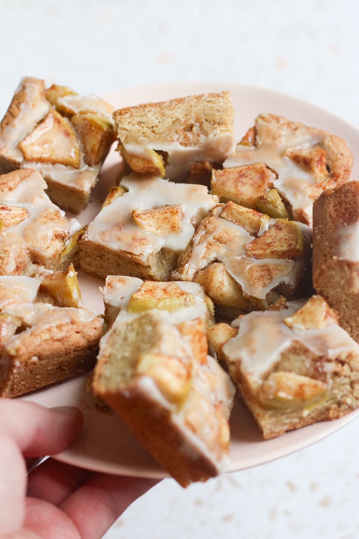 Tyler, author of Schmidty Bakes, holding a pink plate with sliced apple fritter bars.