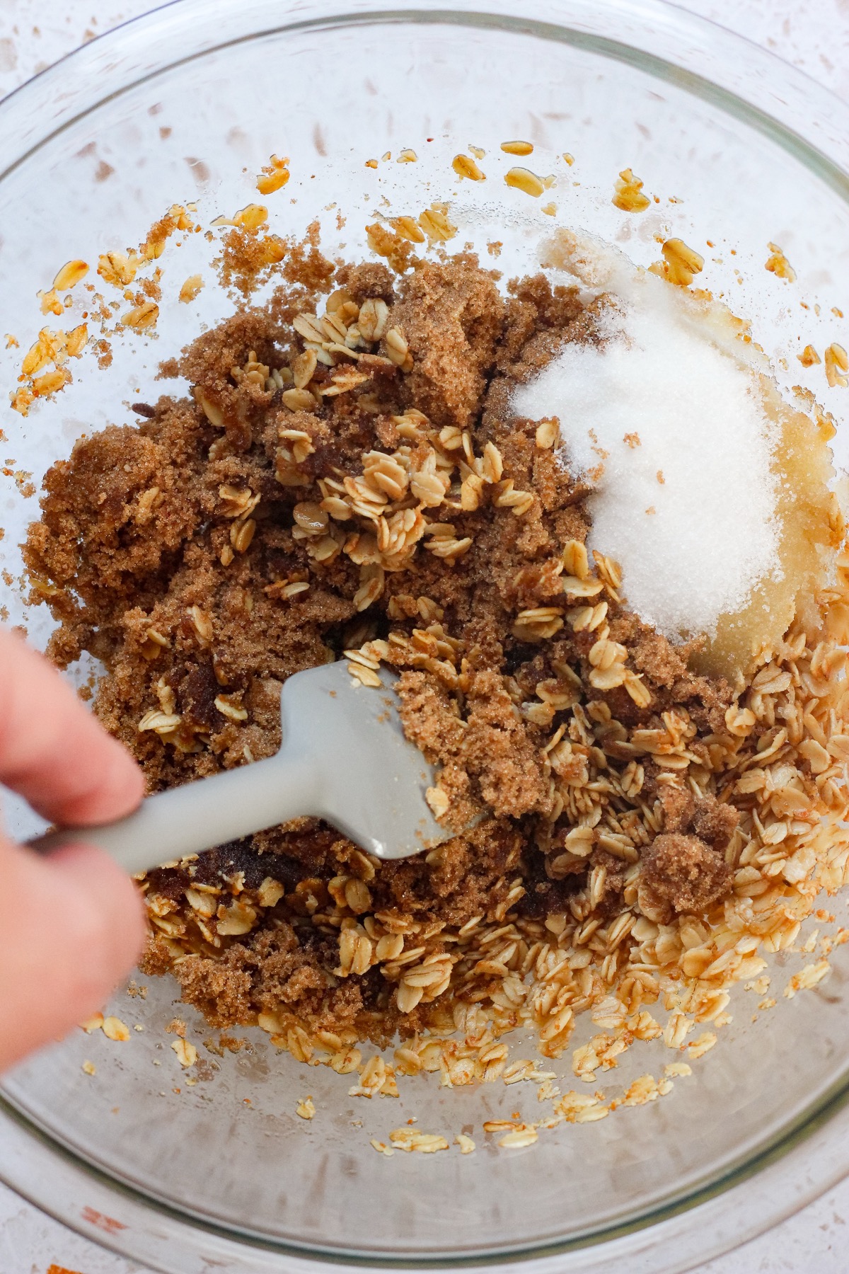 Dark brown sugar and granulated sugar added to brown butter oat mixture in a glass bowl.
