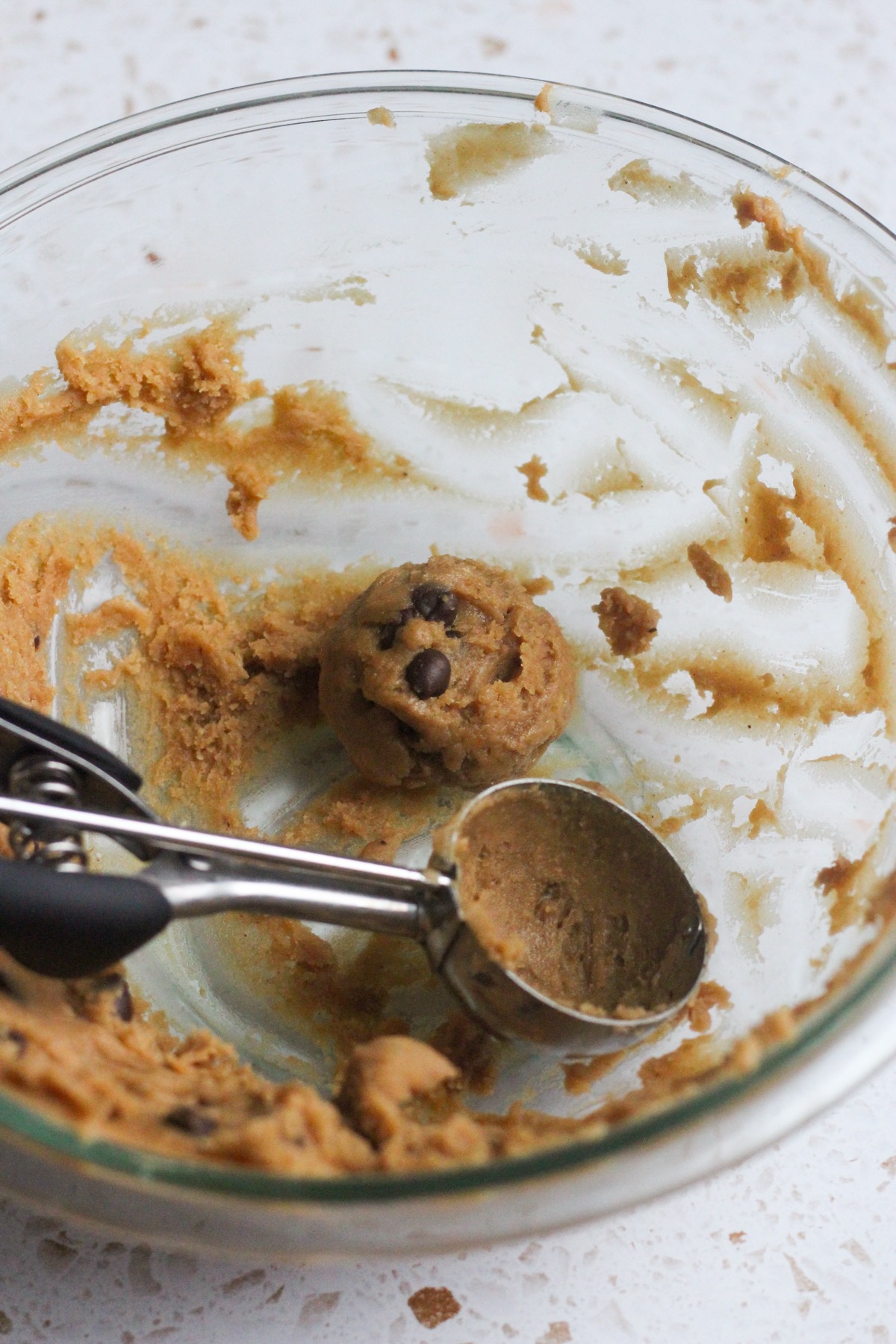 Banana chocolate chip cookie dough in a glass bowl with a cookie scoop.
