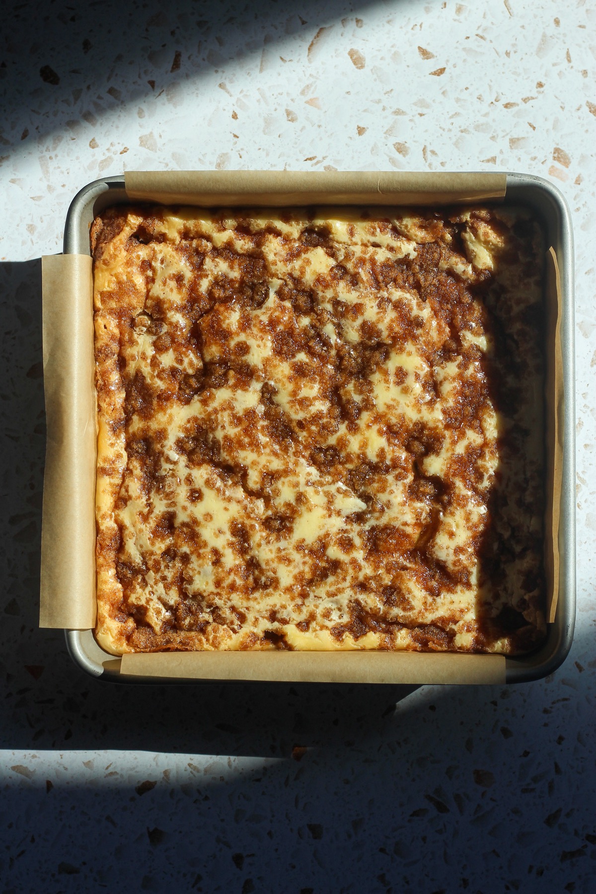 Cinnamon swirl cheesecake bars in sunlight on a backdrop.