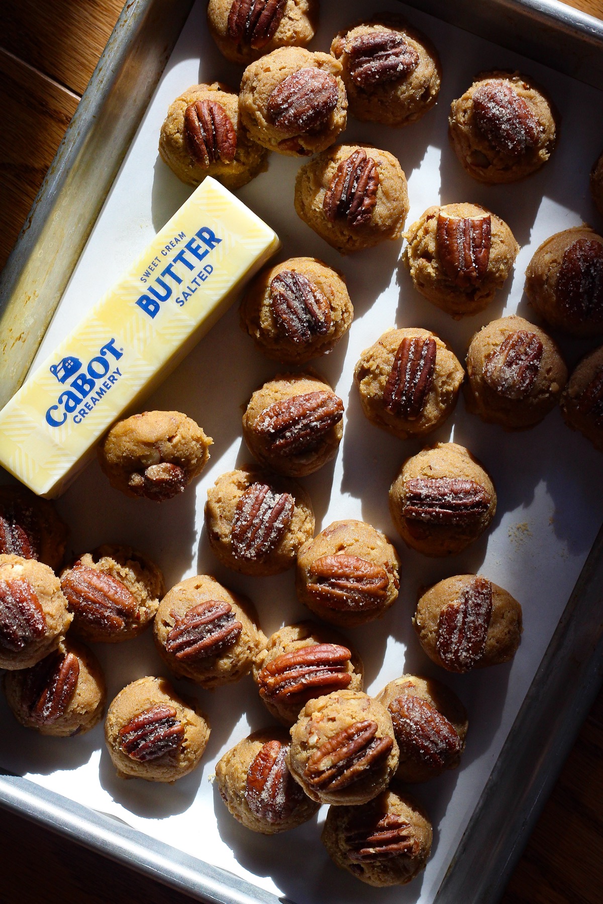 Butter pecan cookie dough on a baking sheet with a stick of Cabot Creamery Salted Butter.