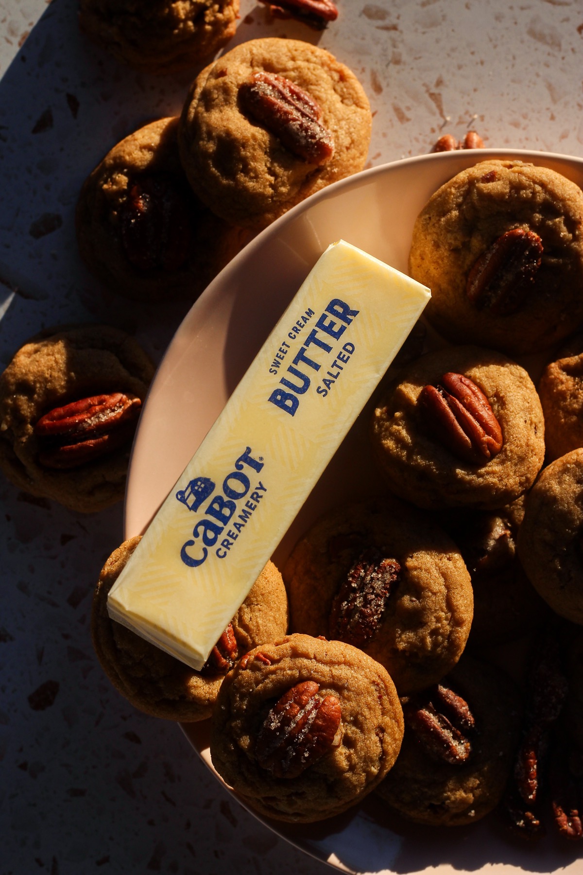 Butter pecan cookies on a pink plate with a stick of Cabot Creamery Salted Butter.