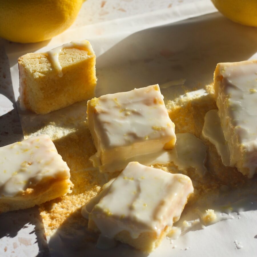 Squares of lemon brownies on a piece of parchment paper in direct sunlight.