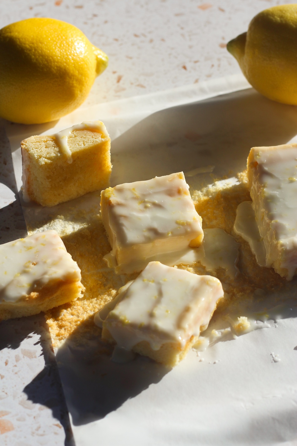Squares of lemon brownies on a piece of parchment paper in direct sunlight.