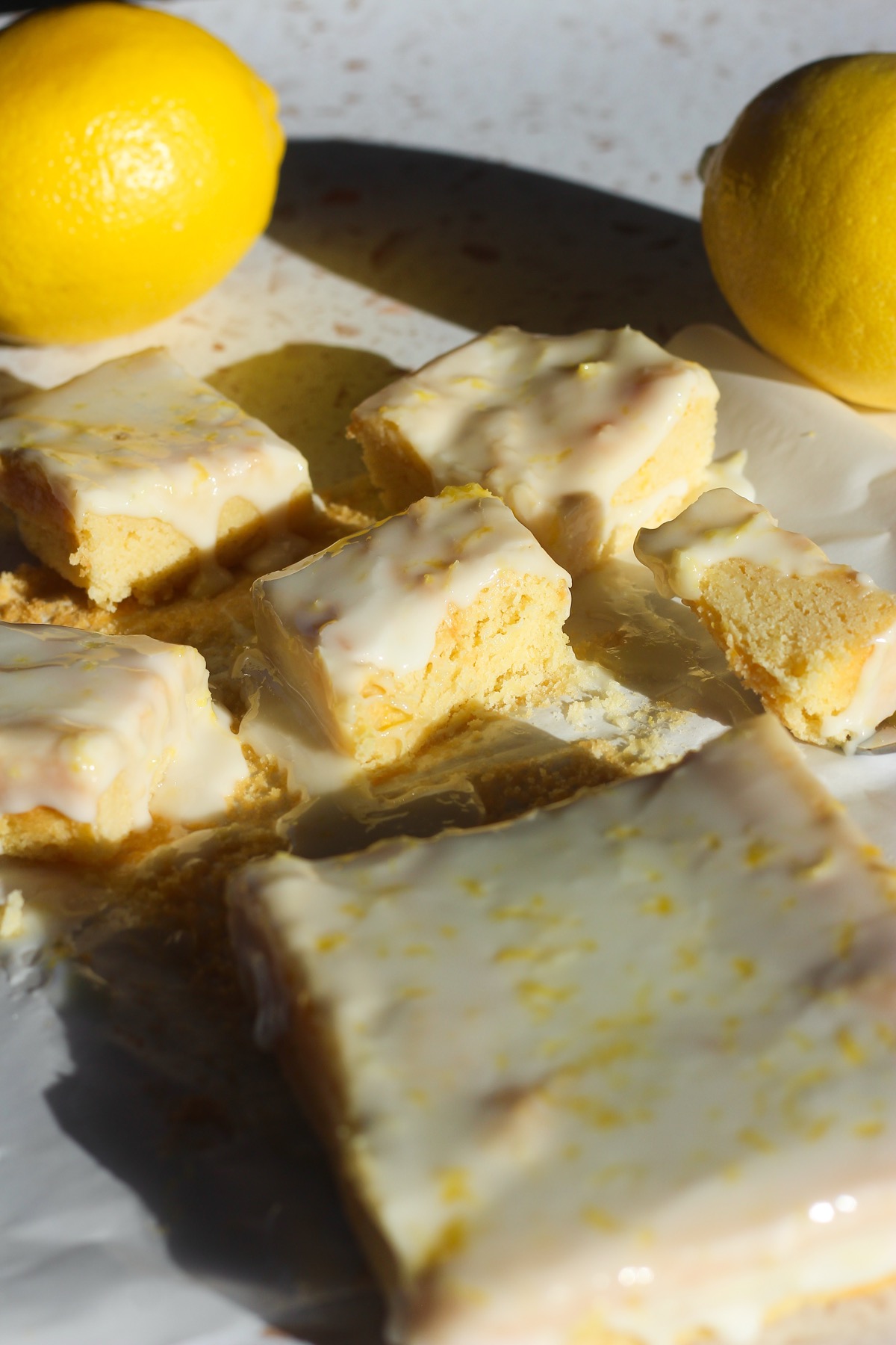 Squares of lemon brownies on a piece of parchment paper in direct sunlight.