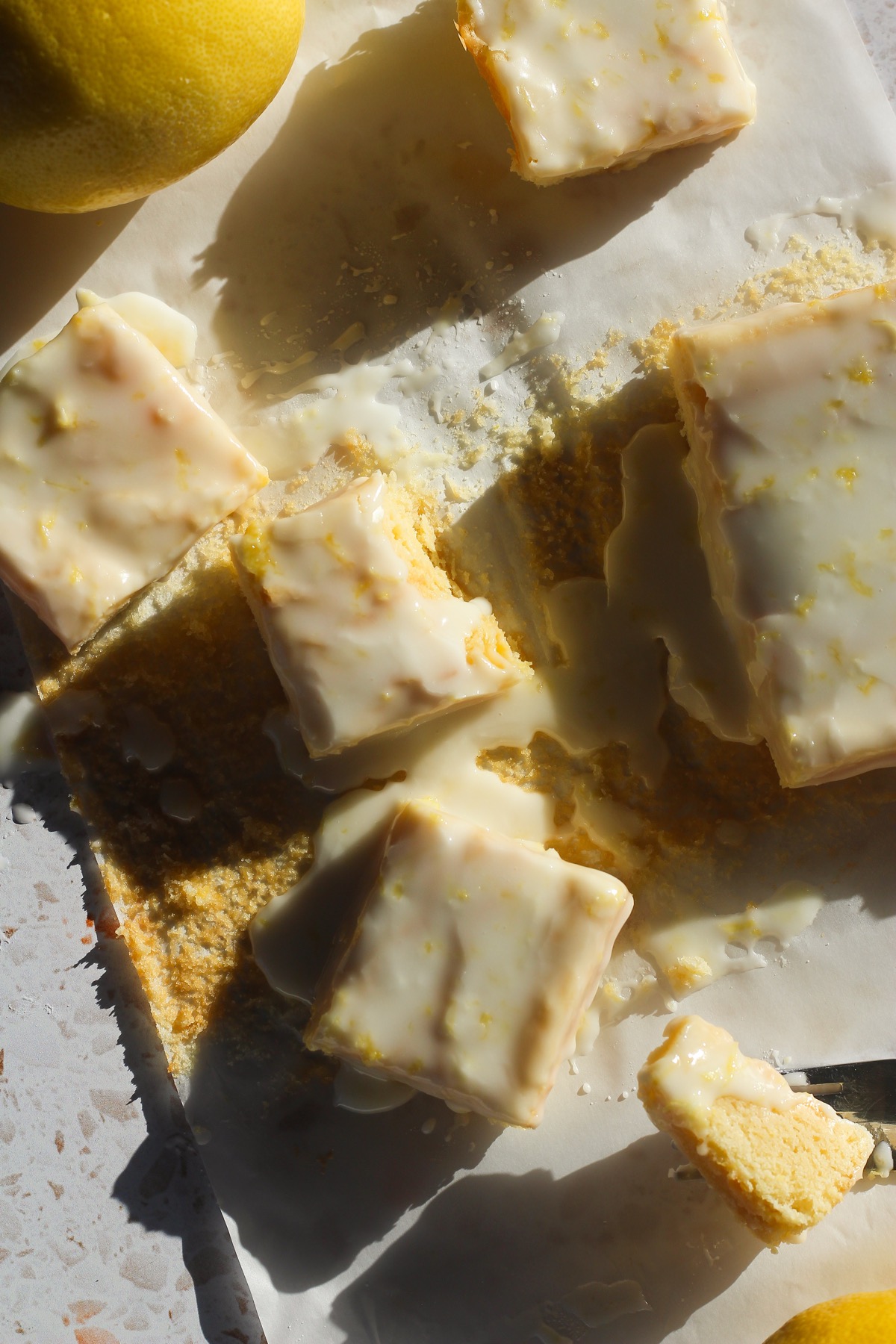 Squares of lemon brownies on a piece of parchment paper in direct sunlight.