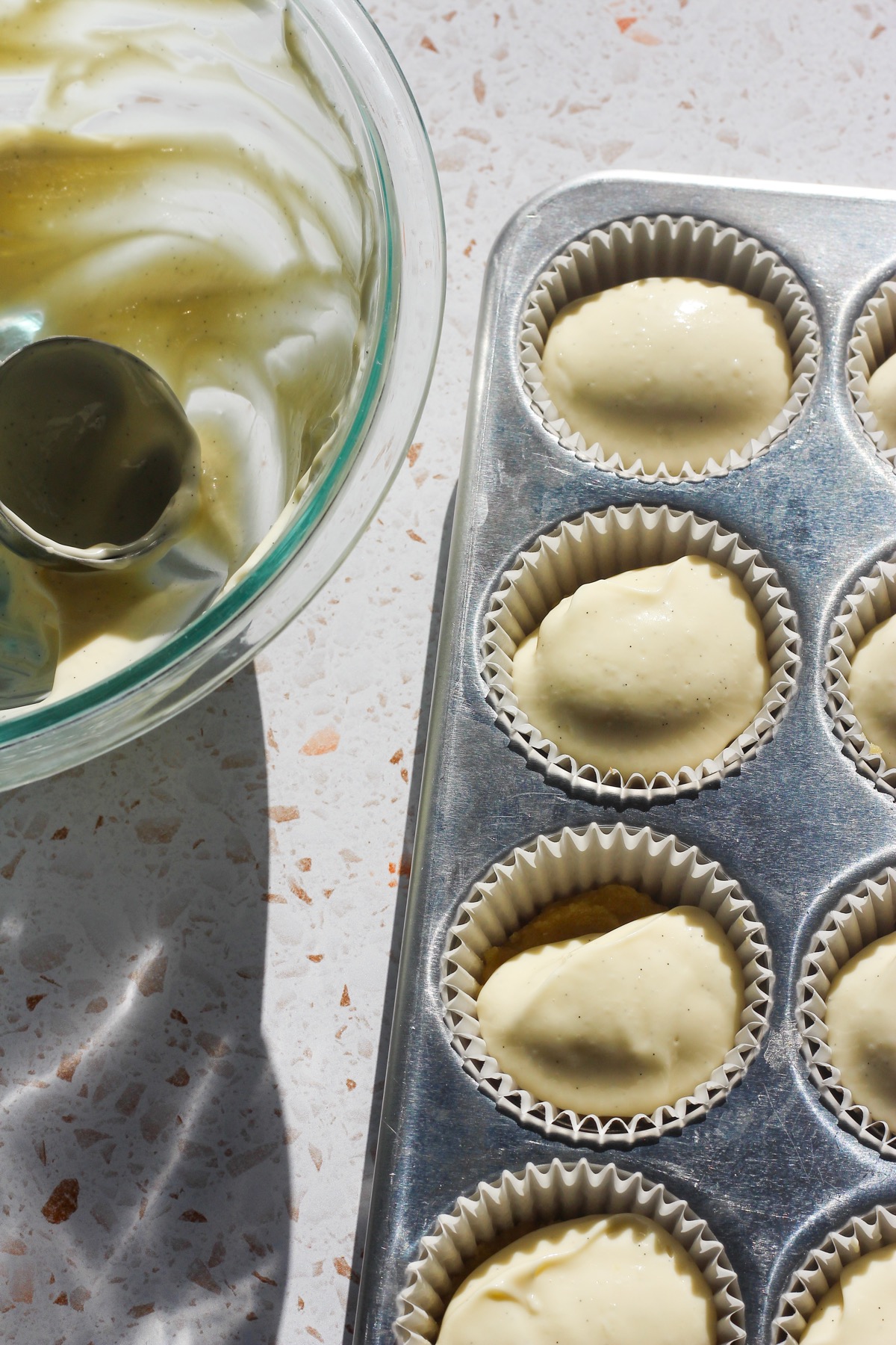Mini almond cheesecake batter being scooped into each muffin liner.