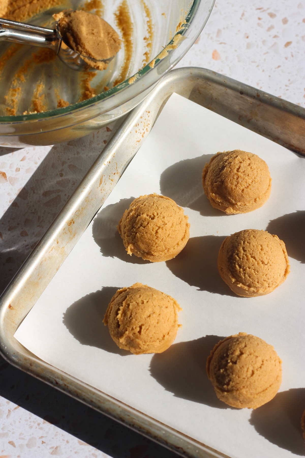 Peanut butter blossoms being scooped out of a glass bowl and onto a baking sheet.
