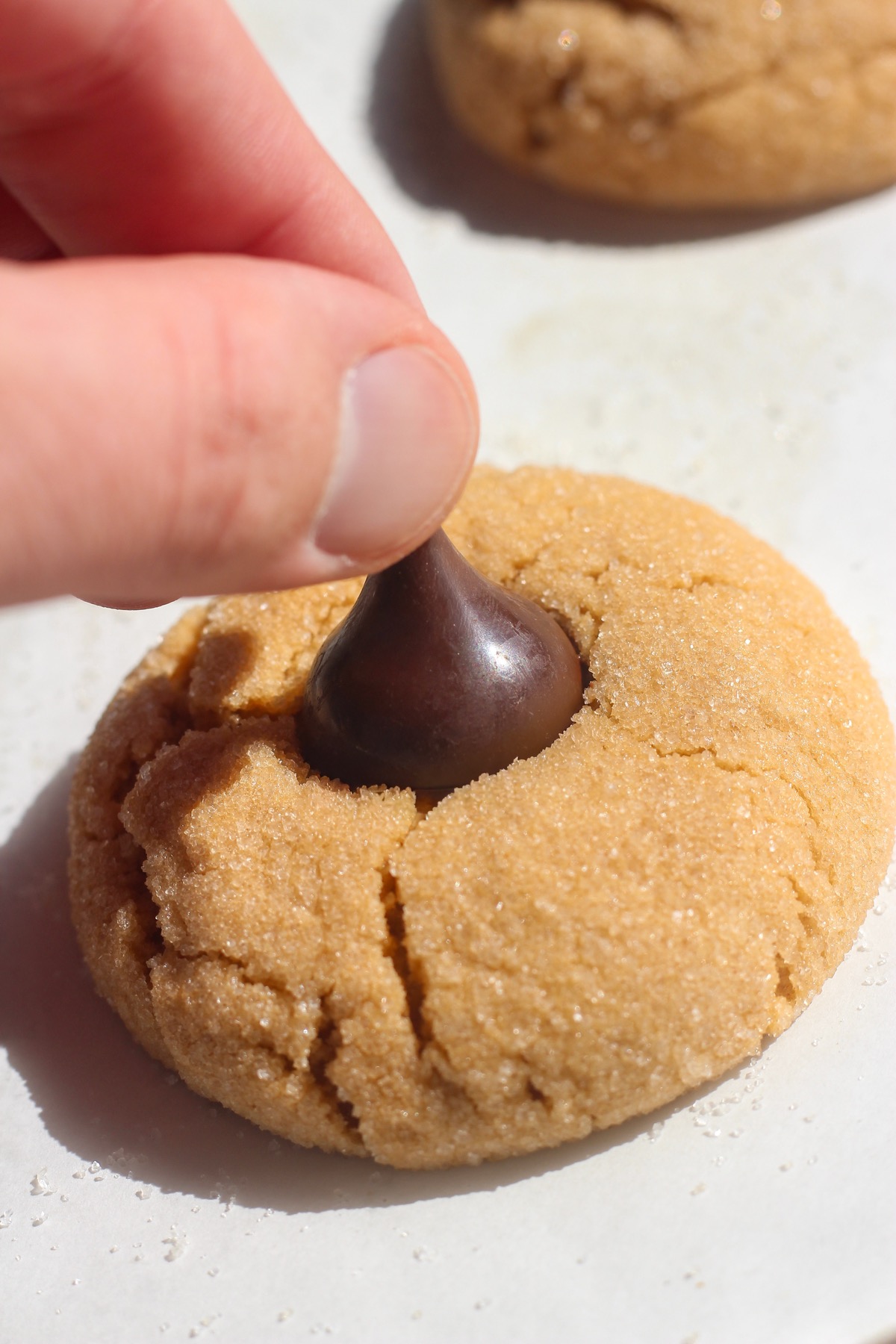 Chocolate kiss being pressed into a peanut butter blossom.