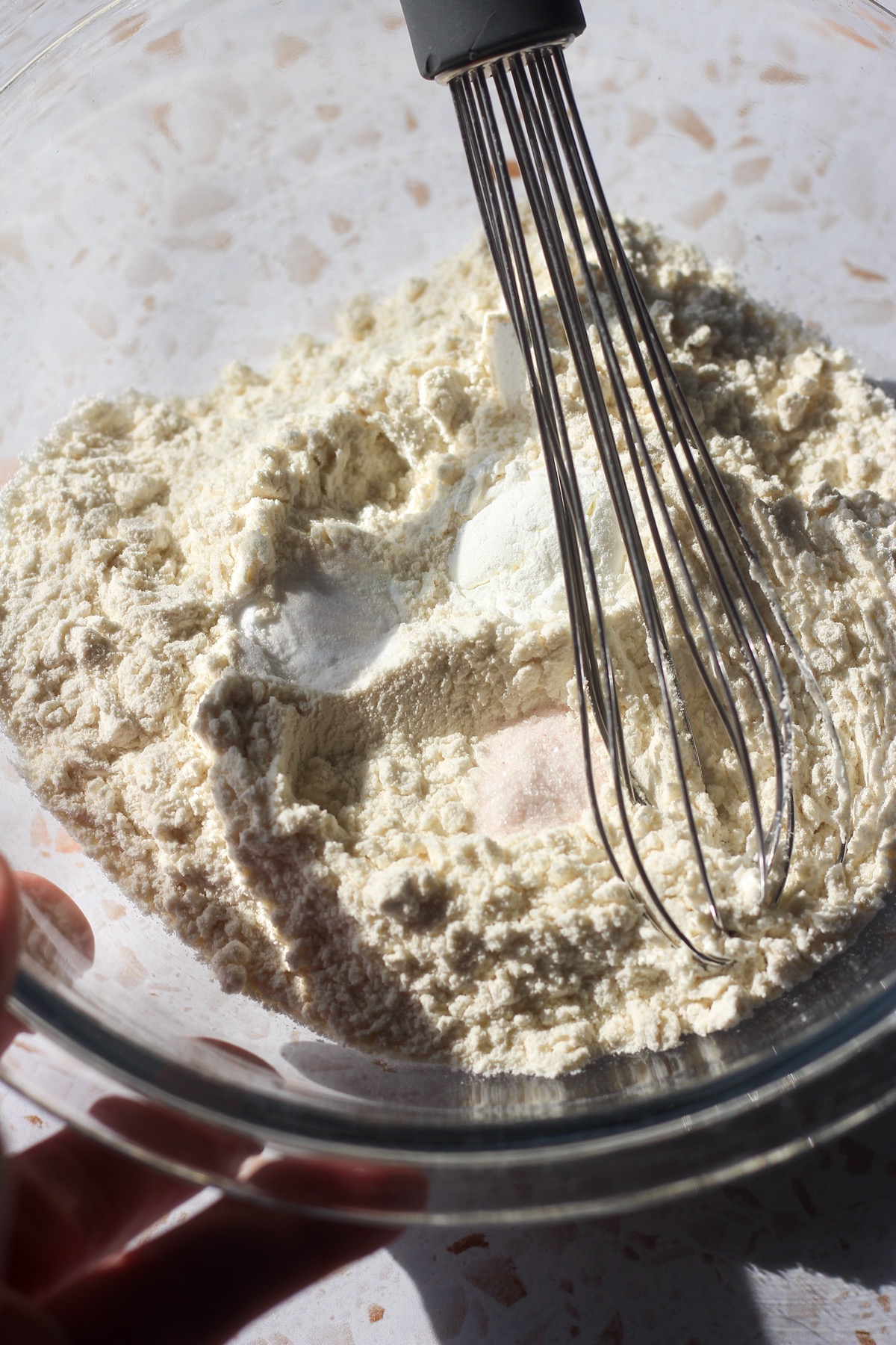 Dry ingredients in a glass bowl with a whisk.
