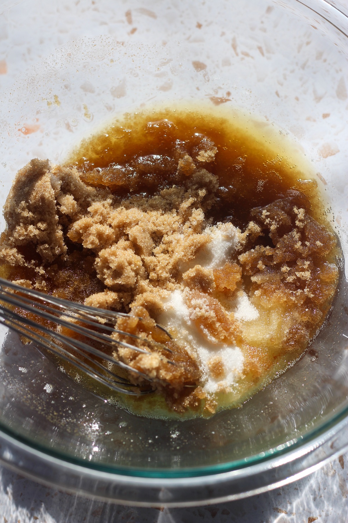 Light brown sugar and granulated sugar added to brown butter in a glass bowl.