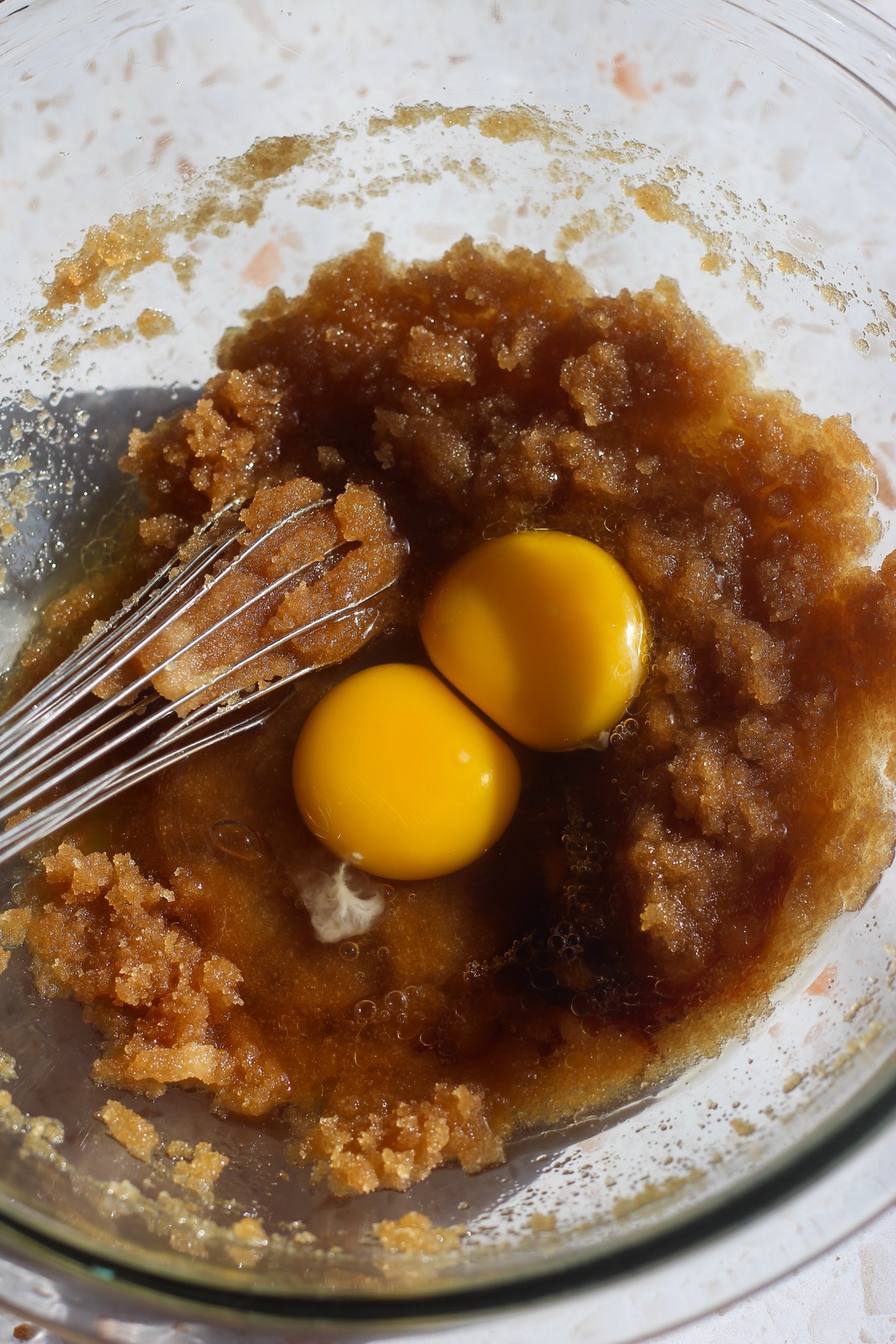 Eggs and vanilla on top of butter mixture in a glass bowl.