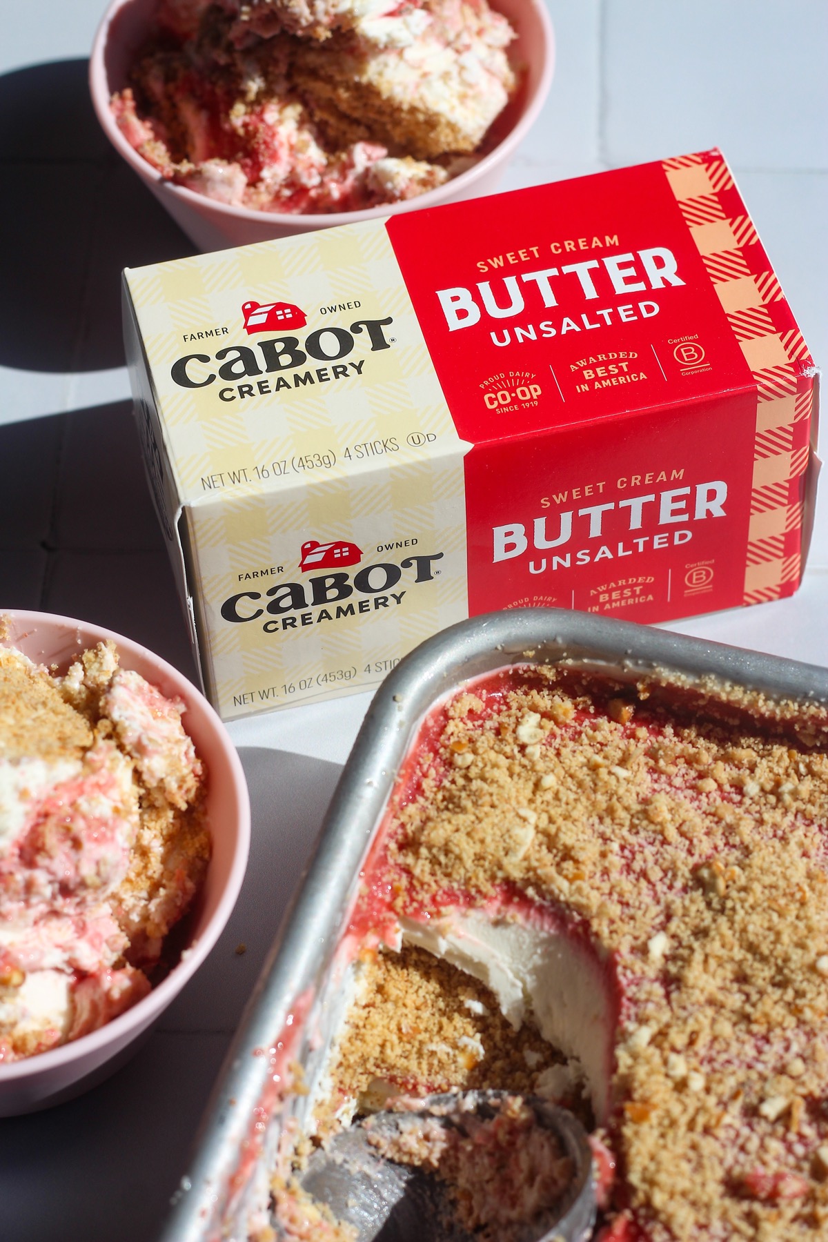 Scoopable strawberry cheesecake in a pink bowl next to pack of Cabot Creamery Unsalted Butter