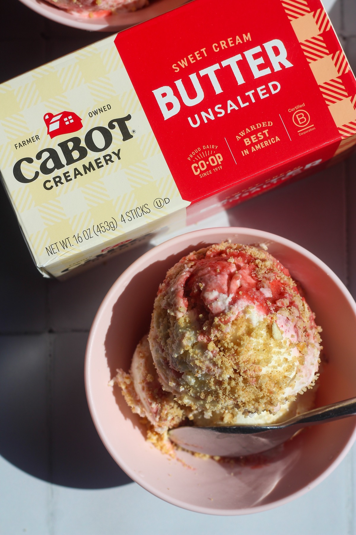 Scoopable strawberry cheesecake in a pink bowl next to pack of Cabot Creamery Unsalted Butter