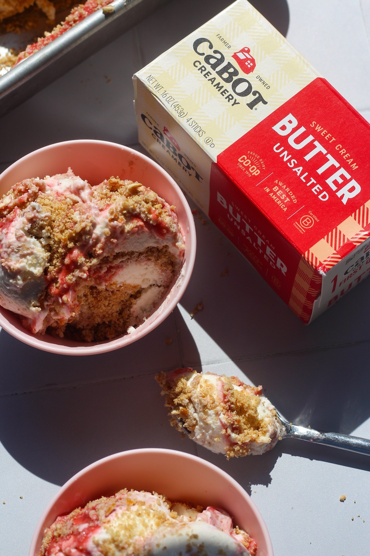 Scoopable strawberry cheesecake in a pink bowl next to pack of Cabot Creamery Unsalted Butter
