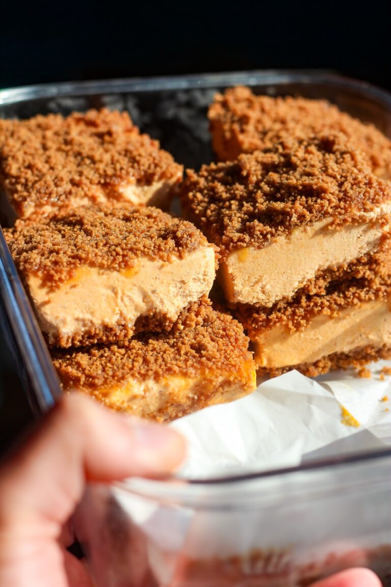 Hand lifting a pan of sliced pumpkin caramel ice cream sandwiches with a gingersnap crust