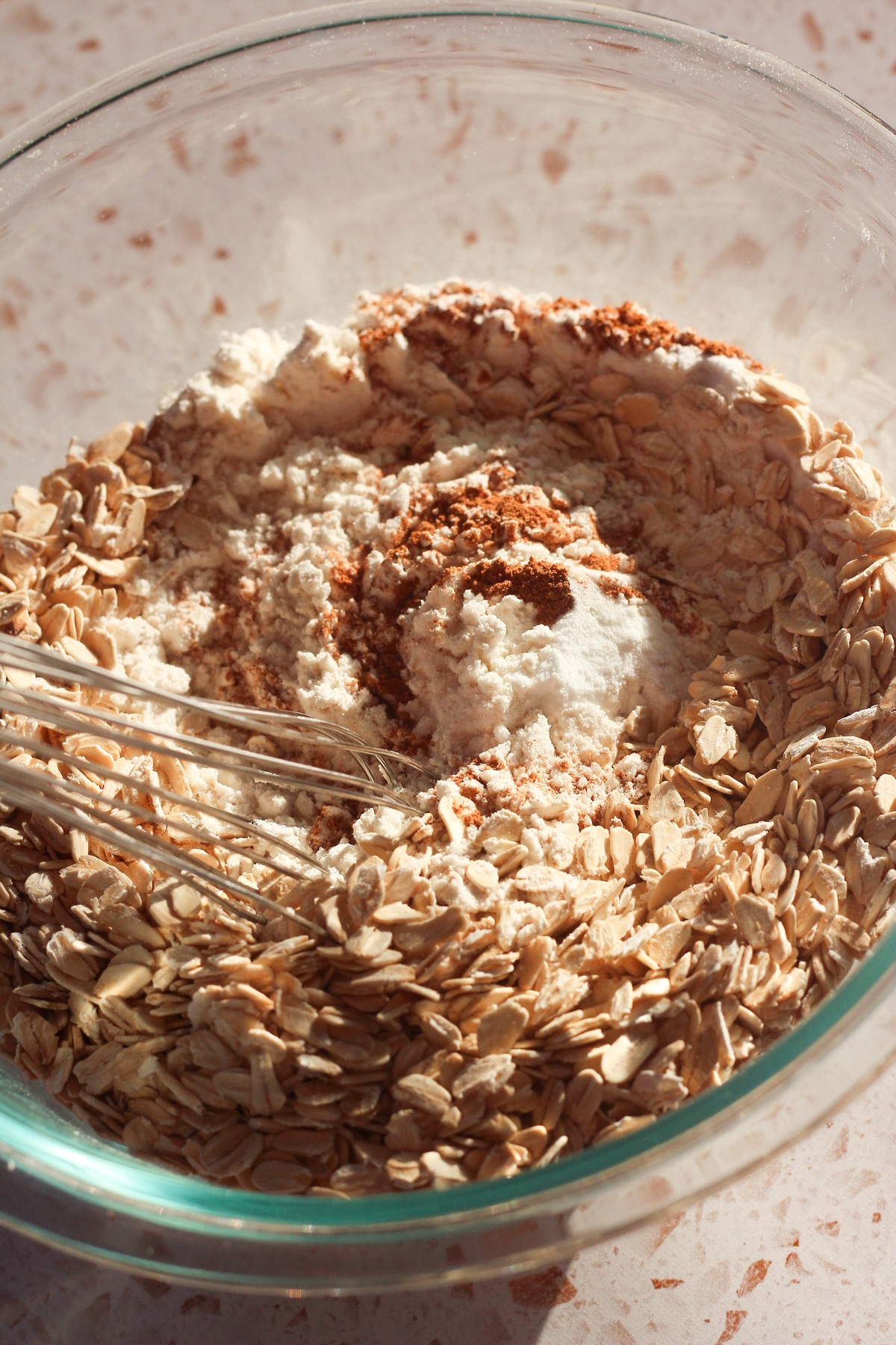 Dry ingredients including oats, flour, and cinnamon whisked together in a glass bowl