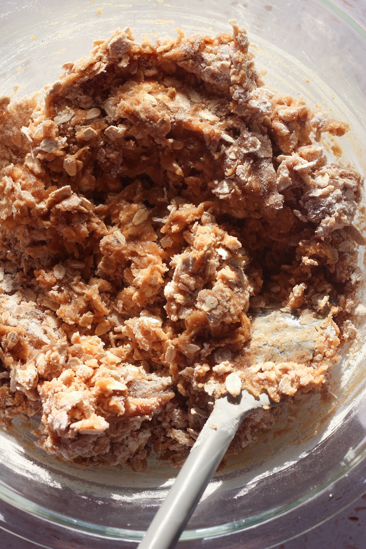 Oatmeal raisin cookie dough being mixed with dry ingredients in a glass bowl