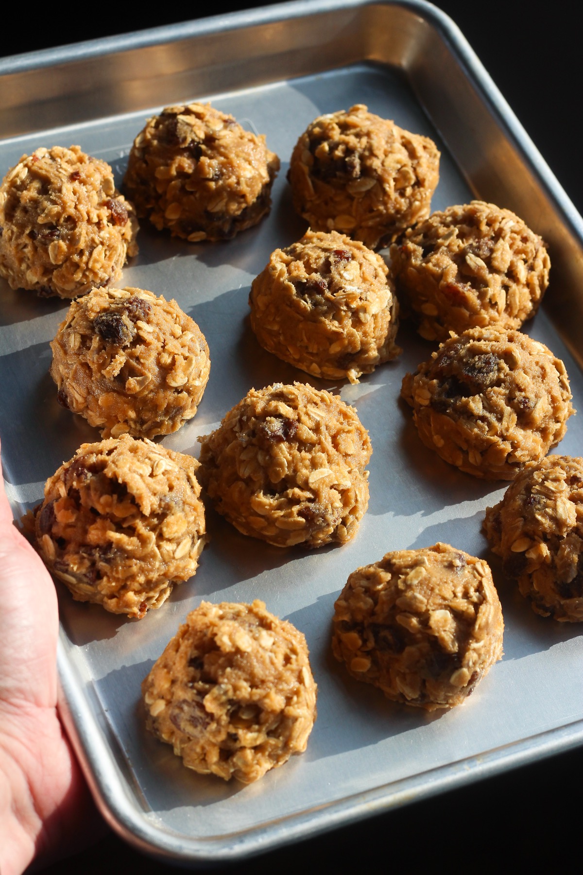 Chilled oatmeal raisin cookie dough balls ready to bake on a metal sheet pan