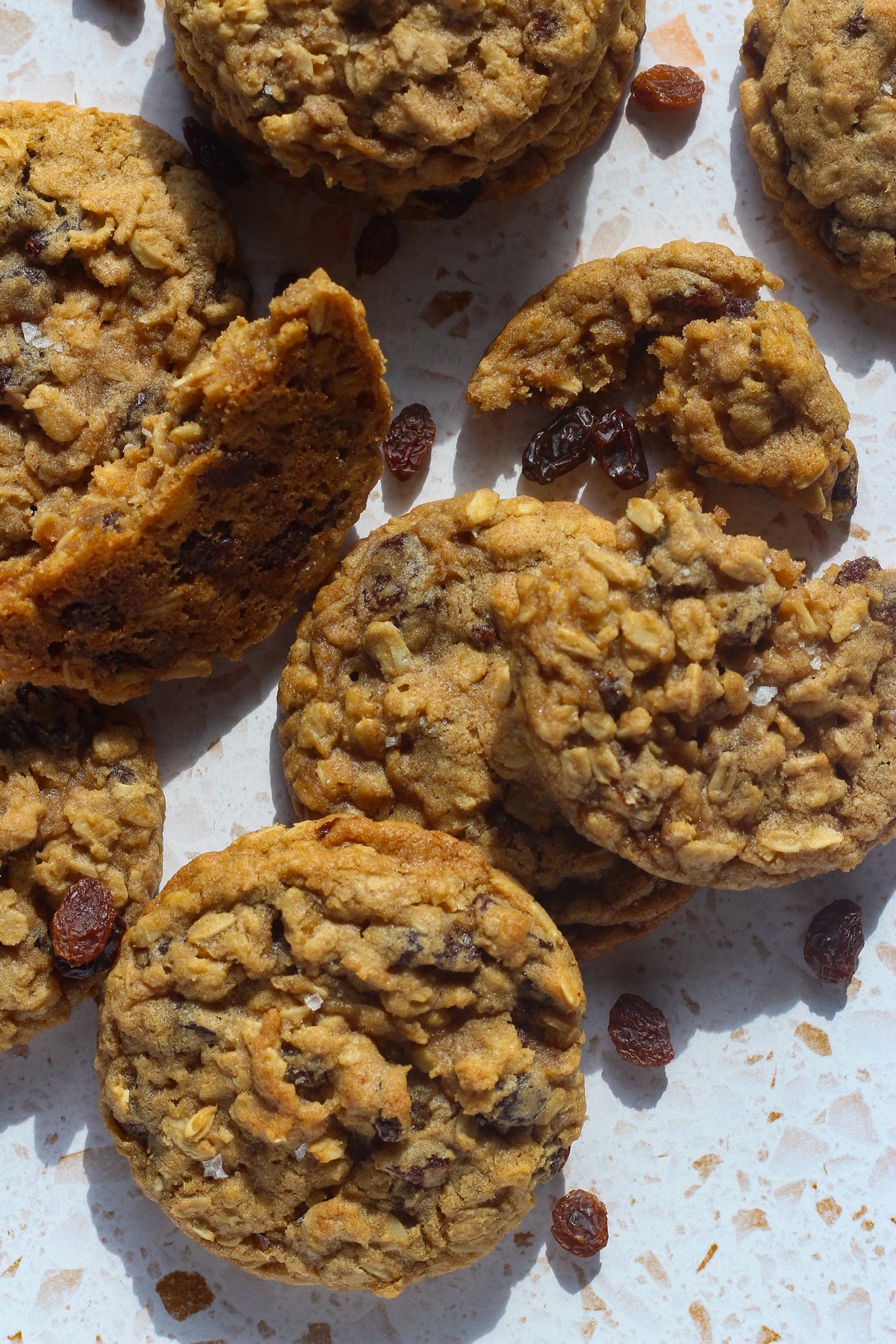 Close-up of oatmeal raisin cookies scattered with loose raisins on a countertop
