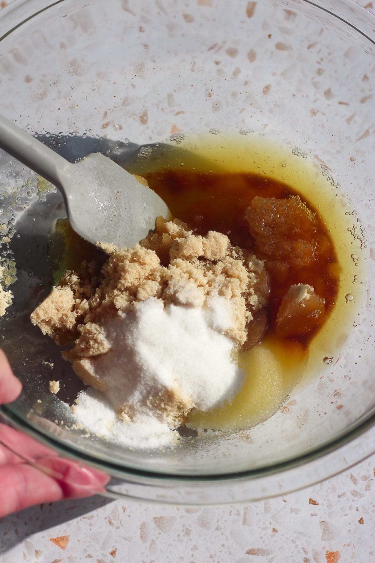 Brown sugar and granulated sugar added to brown butter in a glass bowl with a spatula