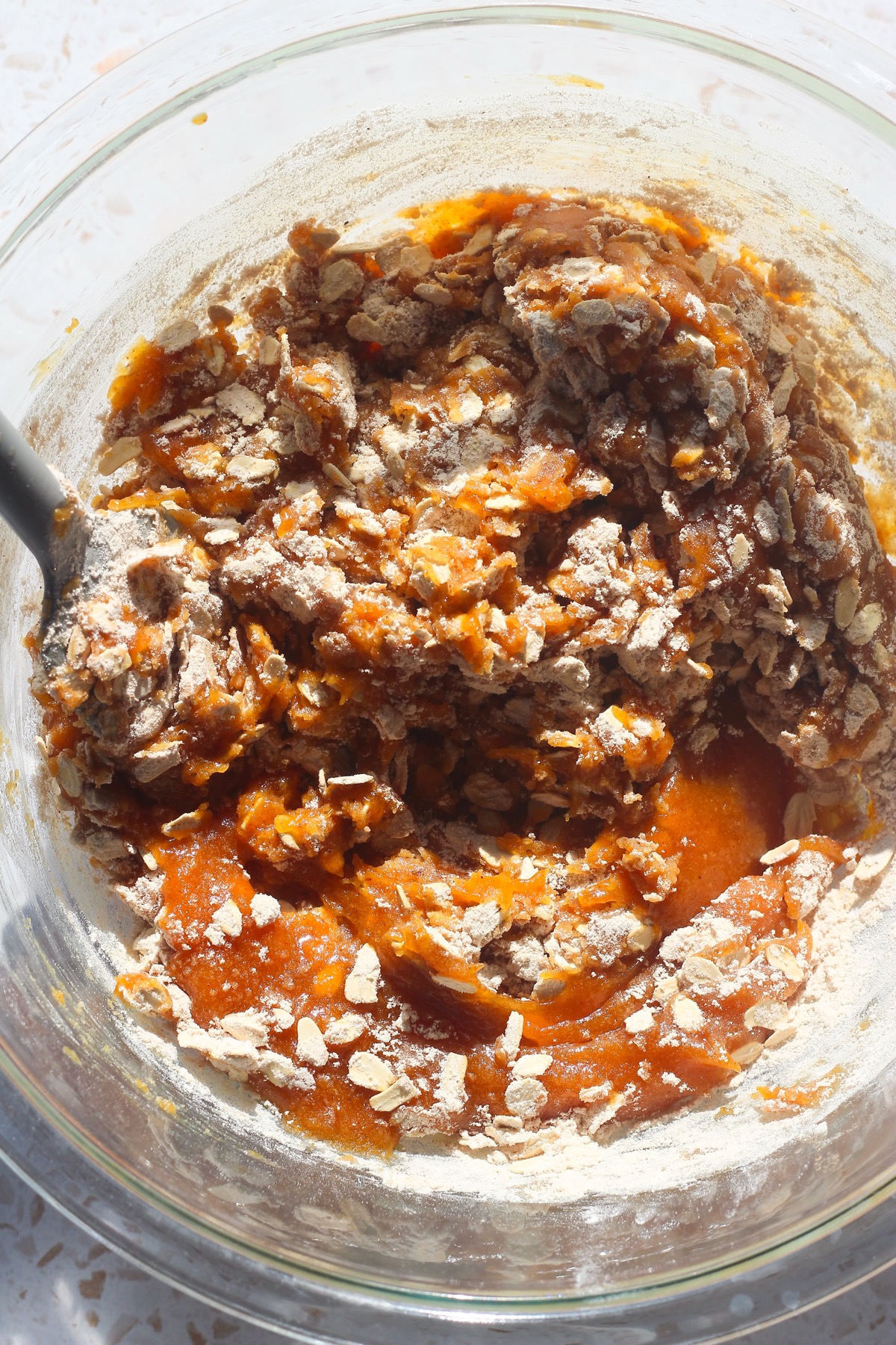 Pumpkin oatmeal cookie dough being folded together with dry ingredients in a glass bowl