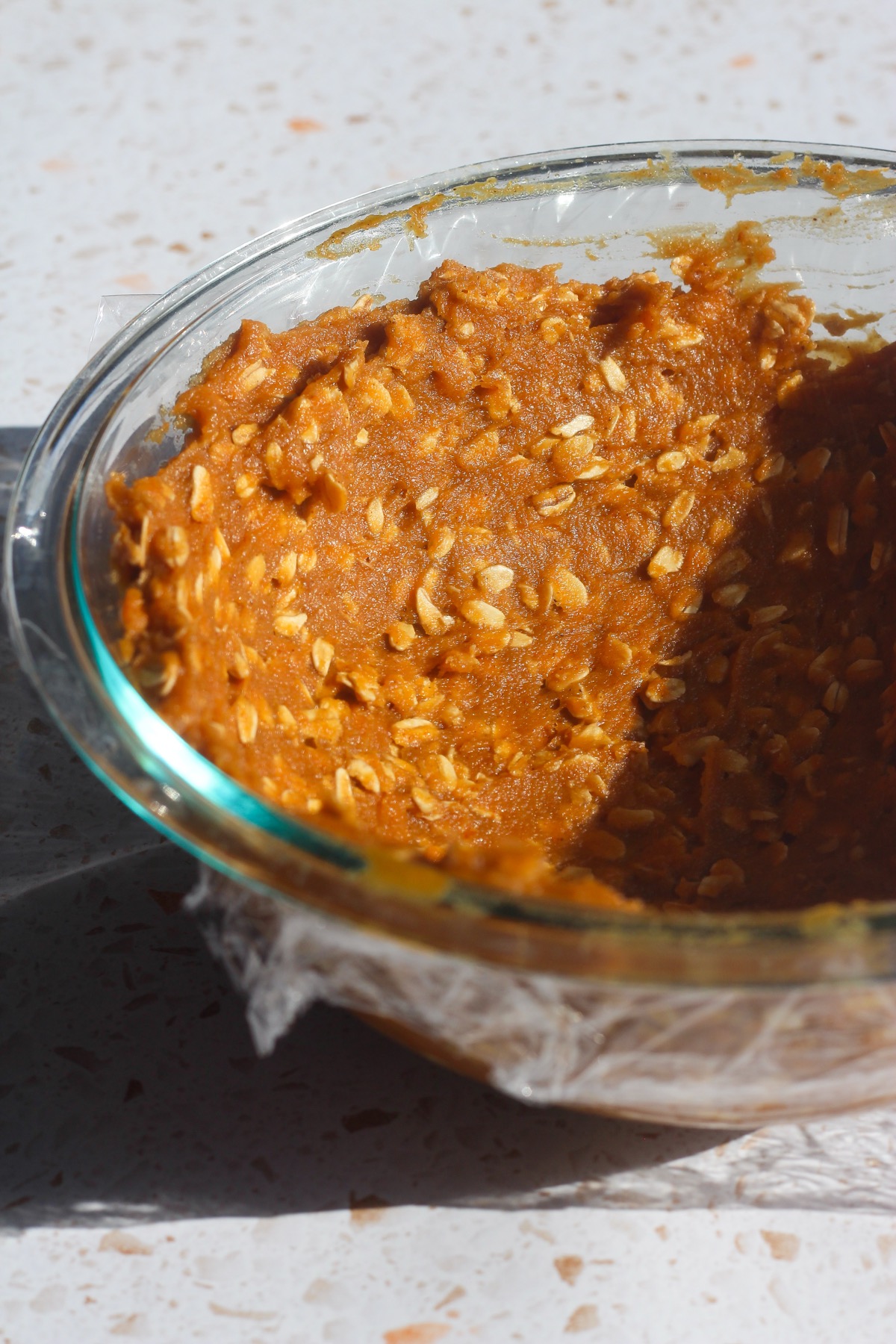 Pumpkin oatmeal cookie dough covered with plastic wrap in a glass bowl for chilling