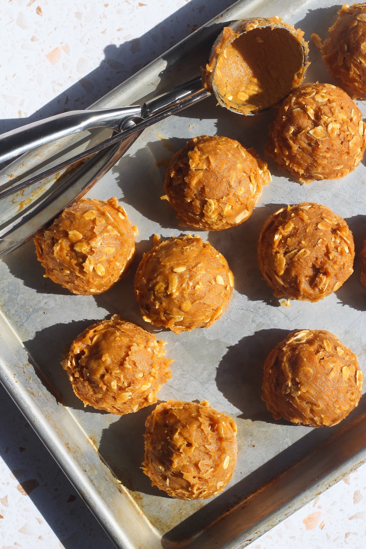 Scooped pumpkin oatmeal cookie dough balls on a baking sheet with a cookie scoop