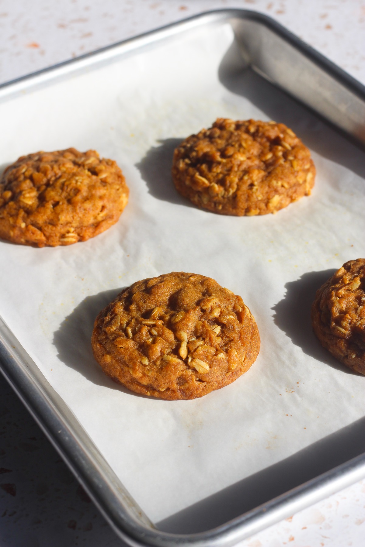 Soft, chewy pumpkin oatmeal cookies with golden edges cooling on a parchment-lined sheet pan