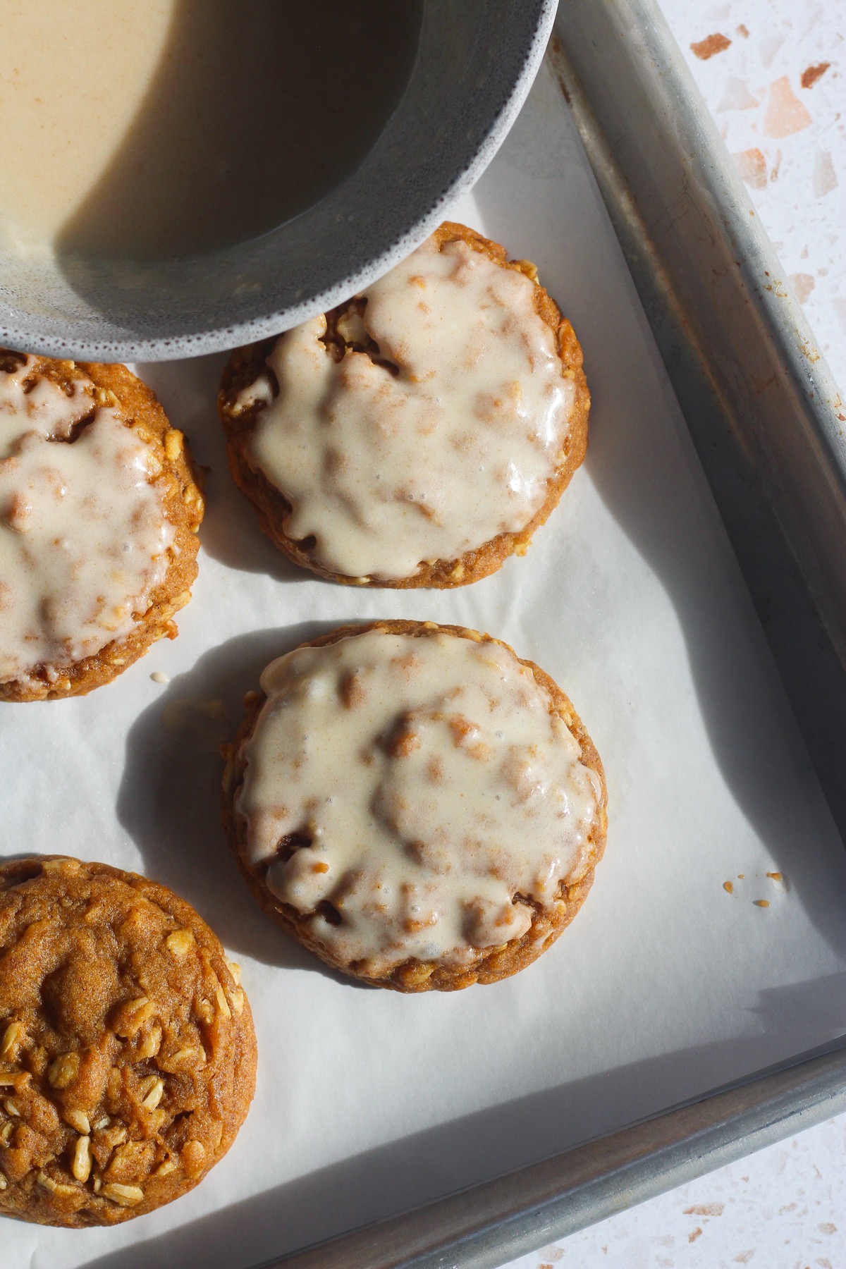 Bowl of brown butter icing next to baked brown butter pumpkin oatmeal cookies on a baking sheet