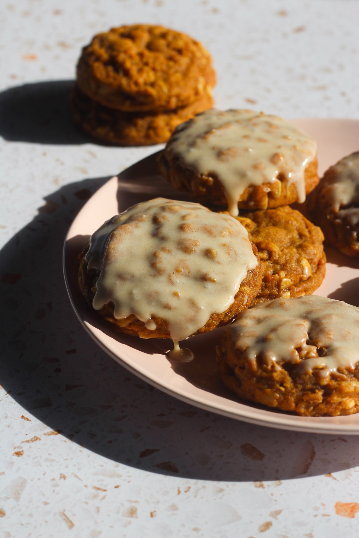 Brown butter pumpkin oatmeal cookies with icing dripping down the sides on a pink plate
