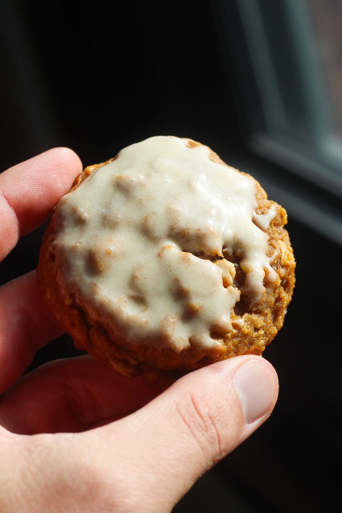 Hand holding an iced brown butter pumpkin oatmeal cookie