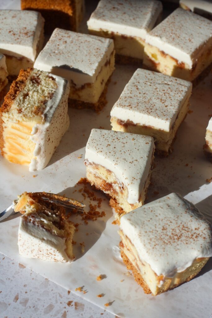 Cinnamon swirl cheesecake bars with a graham cracker crust, topped with whipped cream and dusted with cinnamon, with a bite taken out and a fork nearby